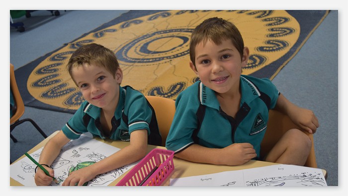 Two Aldavilla public school students colouring in and smiling for the camera.