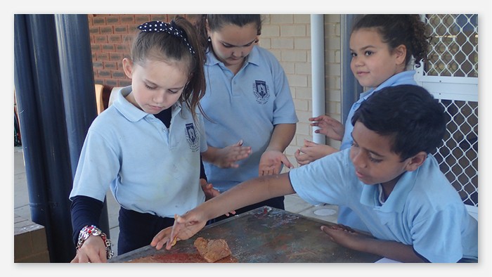 Four young students grinding coloured clay into powder during a cultural art activity.