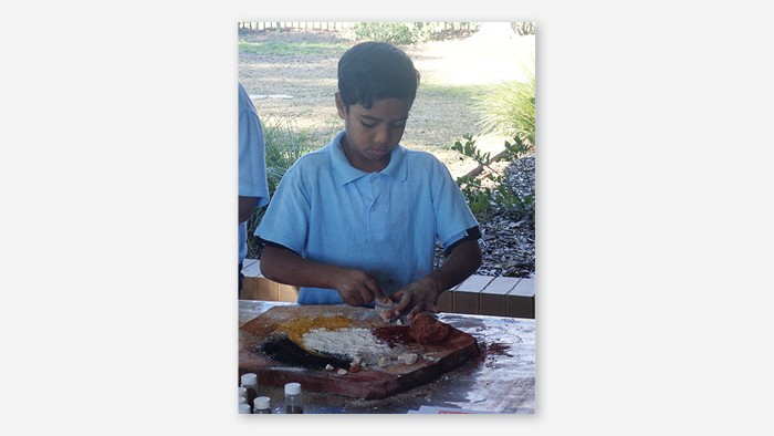A male student grinding coloured clay into powder during a cultural art activity.