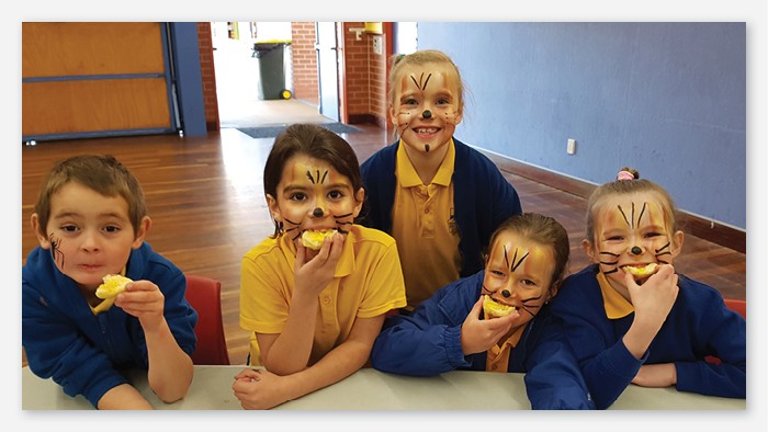 Five Batemans bay public school students eating in their school hall. They have face paint on.