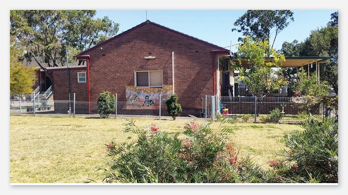 A picture of Doonside public school brick building with Aboriginal art mural. Flowered native bushes in foreground.
