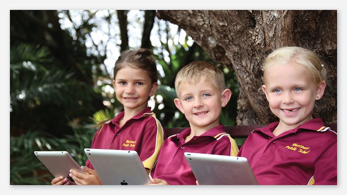 Three young students sitting outside under a tree with iPads.