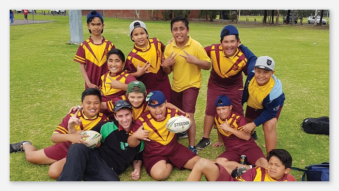 Thirteen students in sports jerseys and holding footballs smile for a team photo on the sports field.