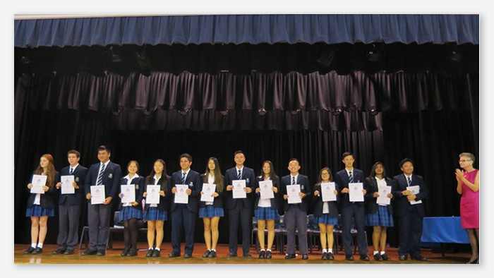 A large group of Sefton High School students stand on a stage holding up their awards.