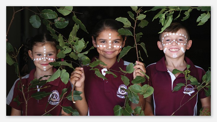 Three students in Taree West uniforms stand among vines with face paint on.