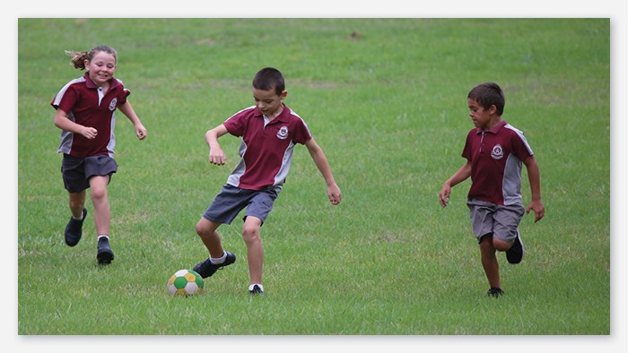 Three Taree West students play soccer out on the field.