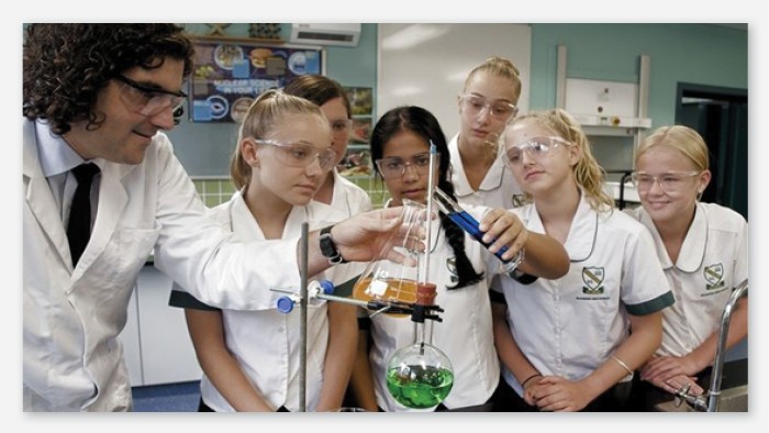 Six students and their teacher combine 2 solutions into a beaker in a science laboratory.