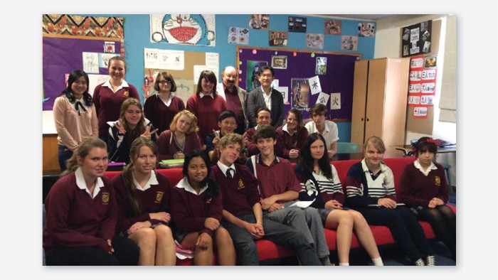 Students and teachers at Armidale High School in a language classroom with cultural references up on the wall. They sit on a couch and smile at the camera.
