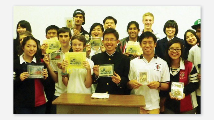 A group of people smiling at the camera. Some of them are holding small artworks depicting Japanese art.