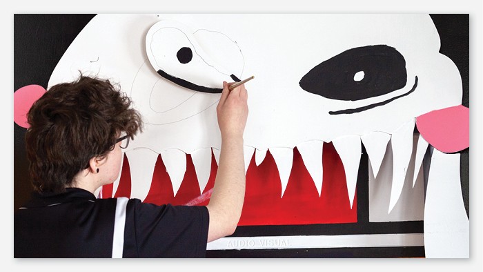 A student painting a large picture of a ghost on the wall.