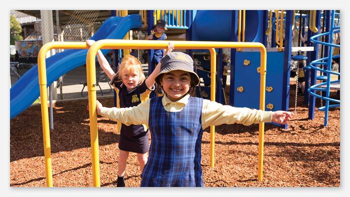 Two young students smiling and playing on a playground.