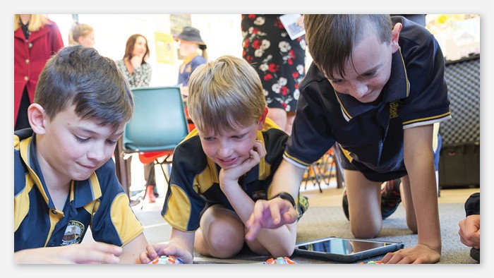Three young students sitting on the floor of a classroom working together on iPad.