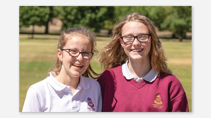 A portrait of two girls in Narrandera school uniform. They are outside in the sun and smiling at the camera.