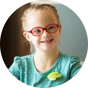 Photo of young girl with glasses smiling at the camera.