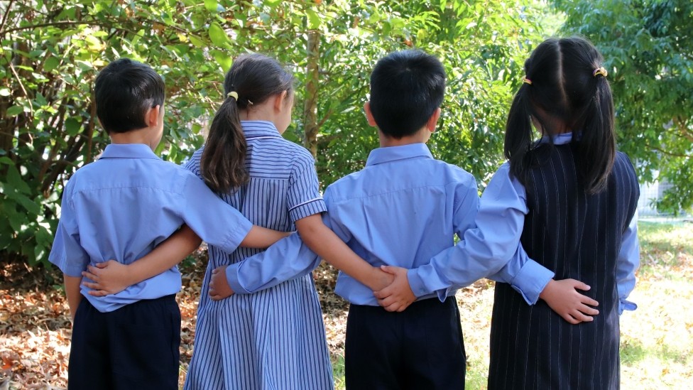 4 primary school students facing away from the camera linking arms.