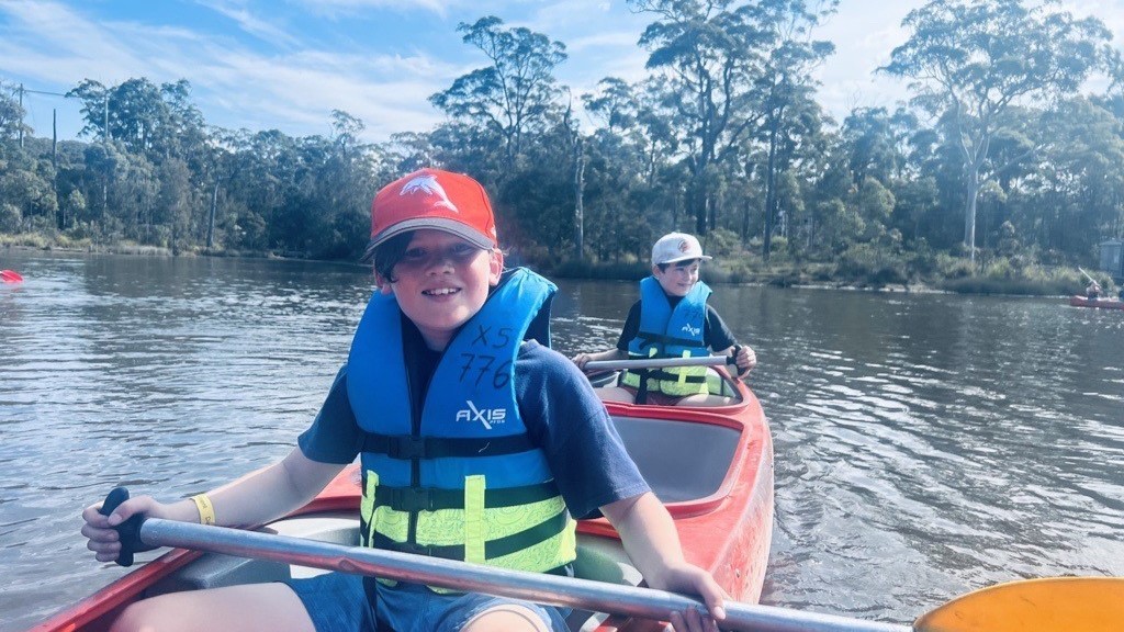 2 primary school male students in a canoe on the river.