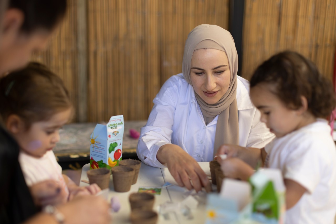 Female educator and two young students playing at an activity table at an early childhood education centre.
