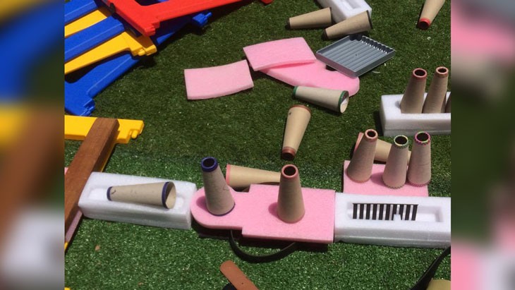 A creation made from reused materials is arranged on fake grass outside. It is made from pieces of pink and white foam, cardboard cones and timbers.