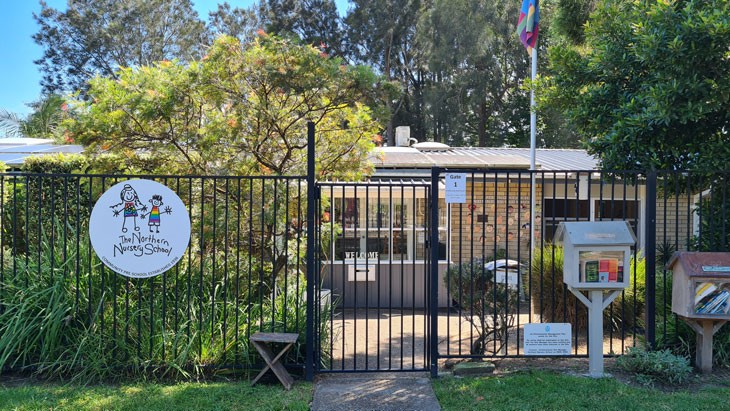 An image of the entrance of an early childhood education service, surrounded by a black fence and two large mailboxes filled with books. The service logo is placed on the fence to welcome the community.