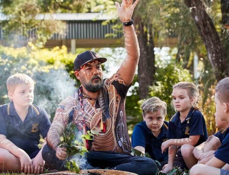 Primary students sitting in a circle with an Aboriginal elder demonstrating a smoking ceremony.