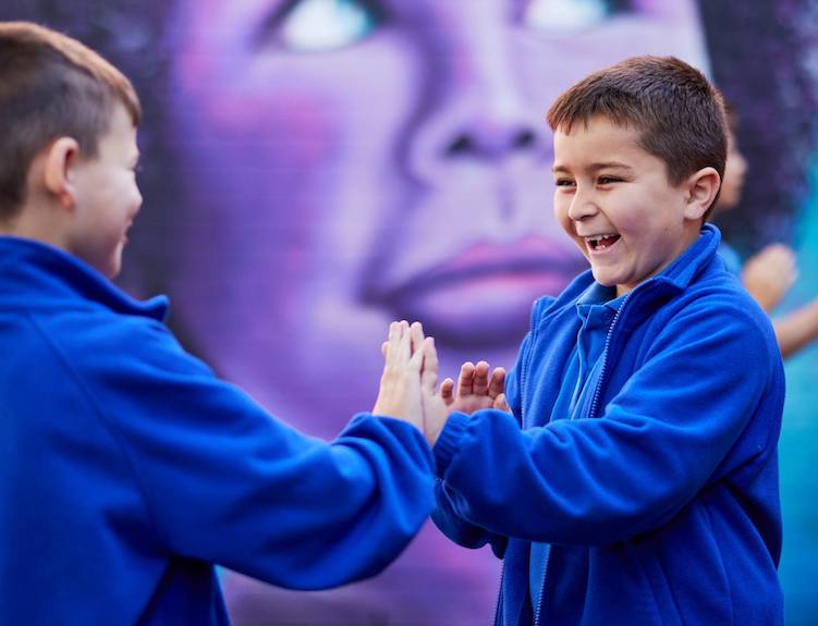 Two boys in blue jumpers playing outside in front of a large mural.