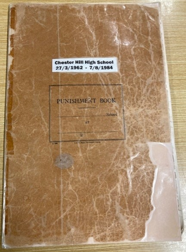 The front cover of a book. It is stained a coffee colour, greatly creased, and the corner has been torn away. The cover has been protected with plastic. There is a printed logo saying Punishment Book and a line to fill in the name of the school. A label has been added with white paper reading Chester Hill High School 1962 to 1984