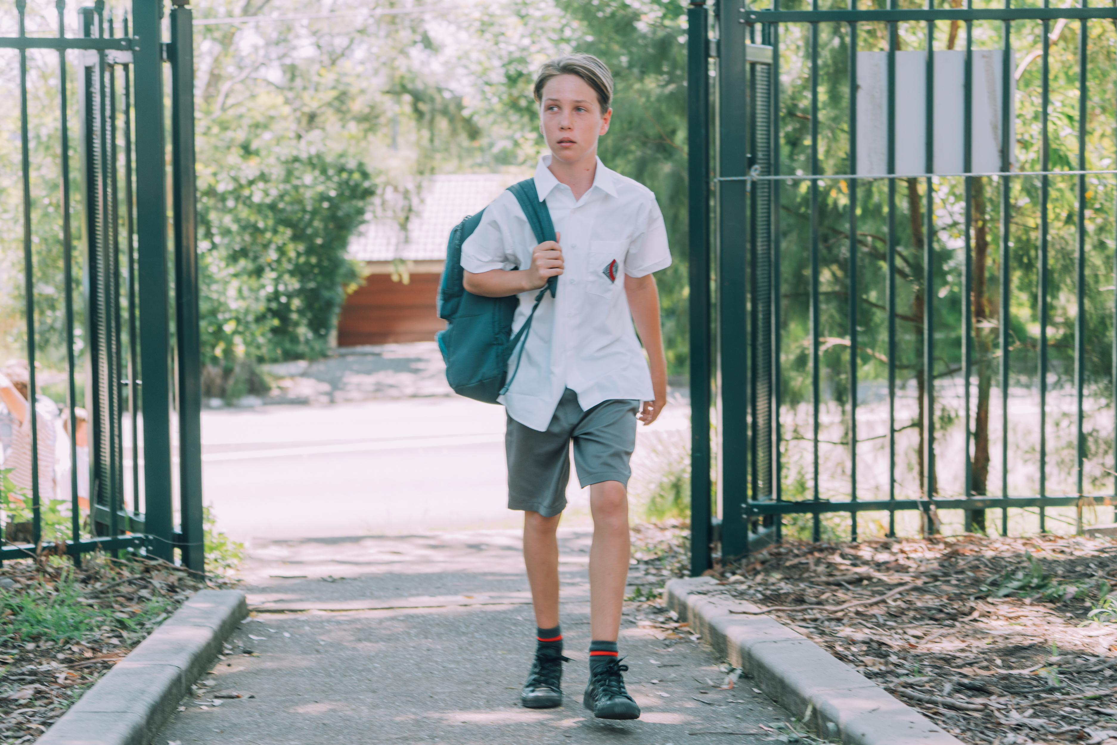 Male primary student walking into school with backpack.