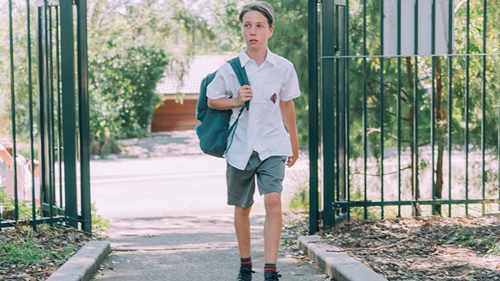 School boy walking into school with backpack.