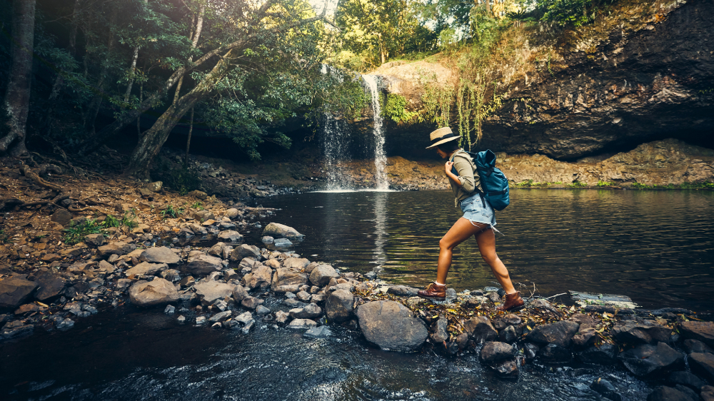 Woman with backpack walking across stones in creek