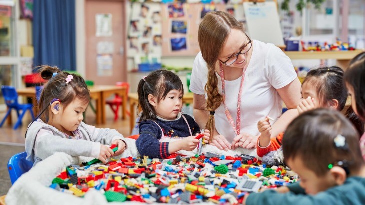 An educator and five children sitting at a table playing with Lego blocks inside an early childhood education centre.