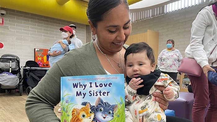 A woman is holding a baby and a book titled Why I Love My Sister
