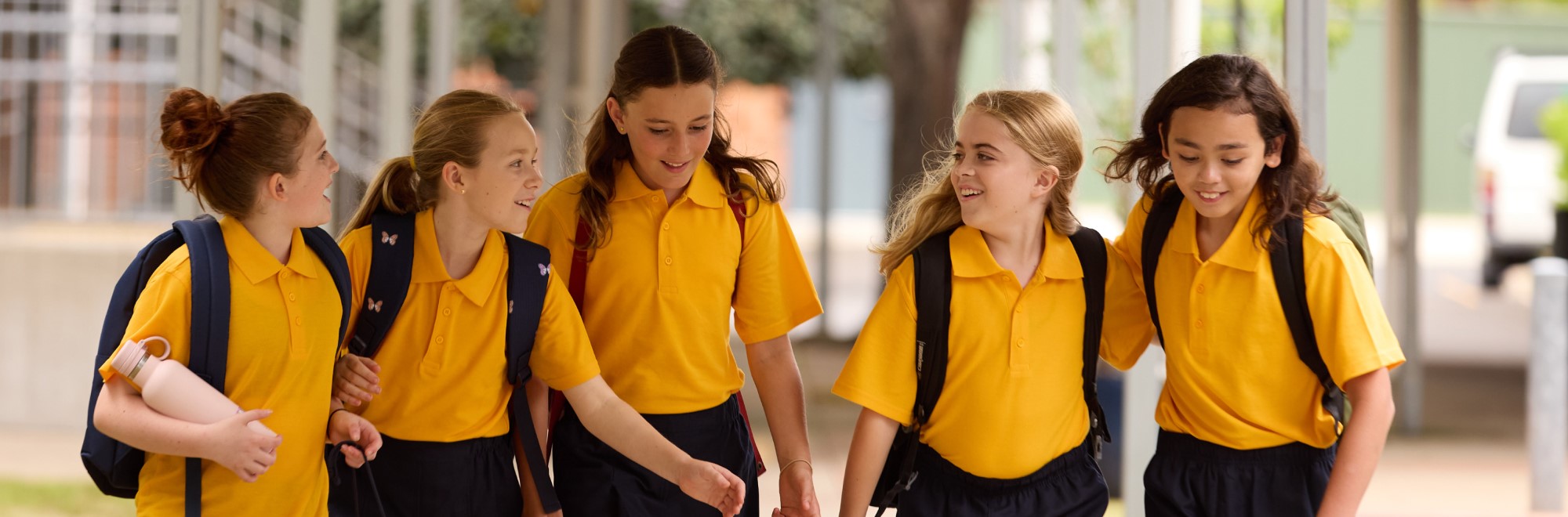 Five female students in yellow school polo shirts walking and talking happily. 