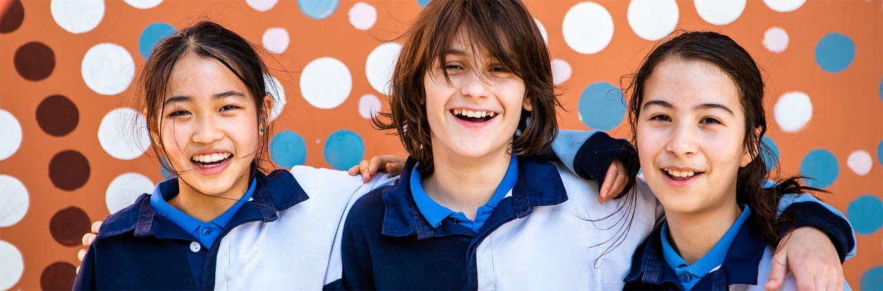 3 teenage students smiling at the camera in front of a mural