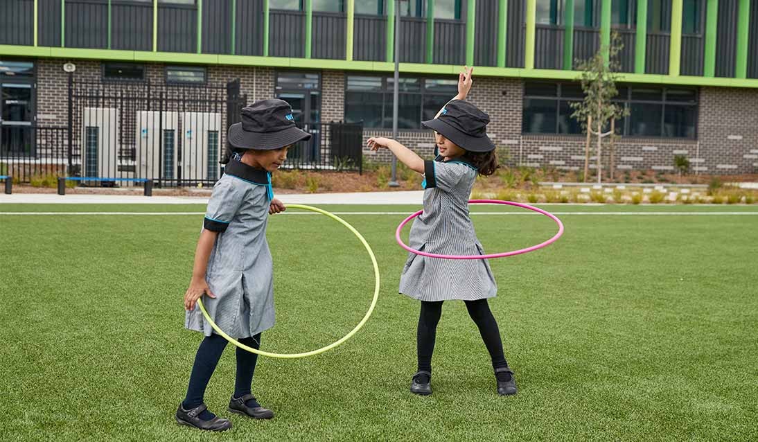 Two girls playing with hula hoops on grass.
