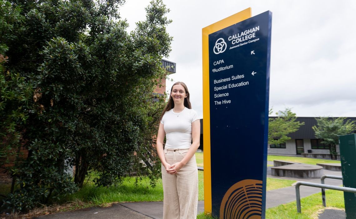 A student standing in front of a school sign.