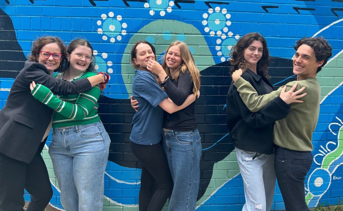 Students standing with their teacher in front of a blue mural.