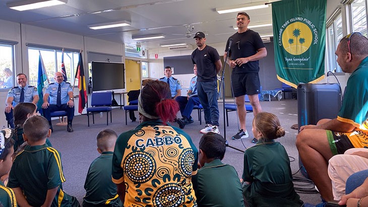 Latrell Mitchell and Cody Walker standing to talk to seated students and staff at Cabbage Tree Island Public School.