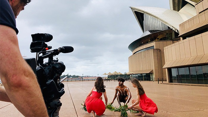 A cameraman in the foreground films Aboriginal student dancers.