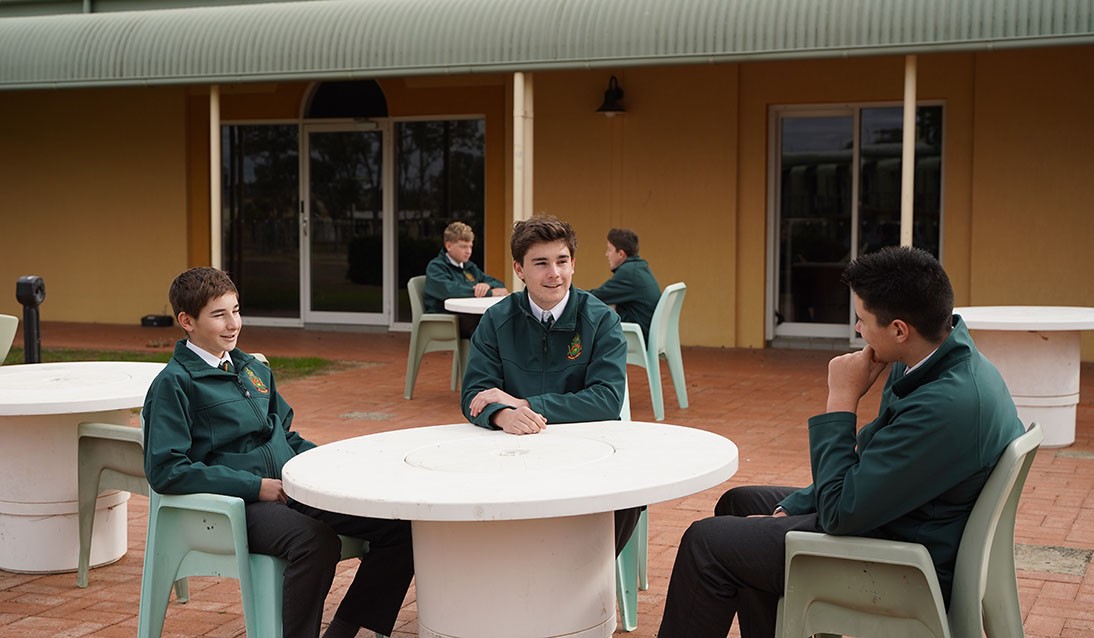 Three male students sitting around a table outside.
