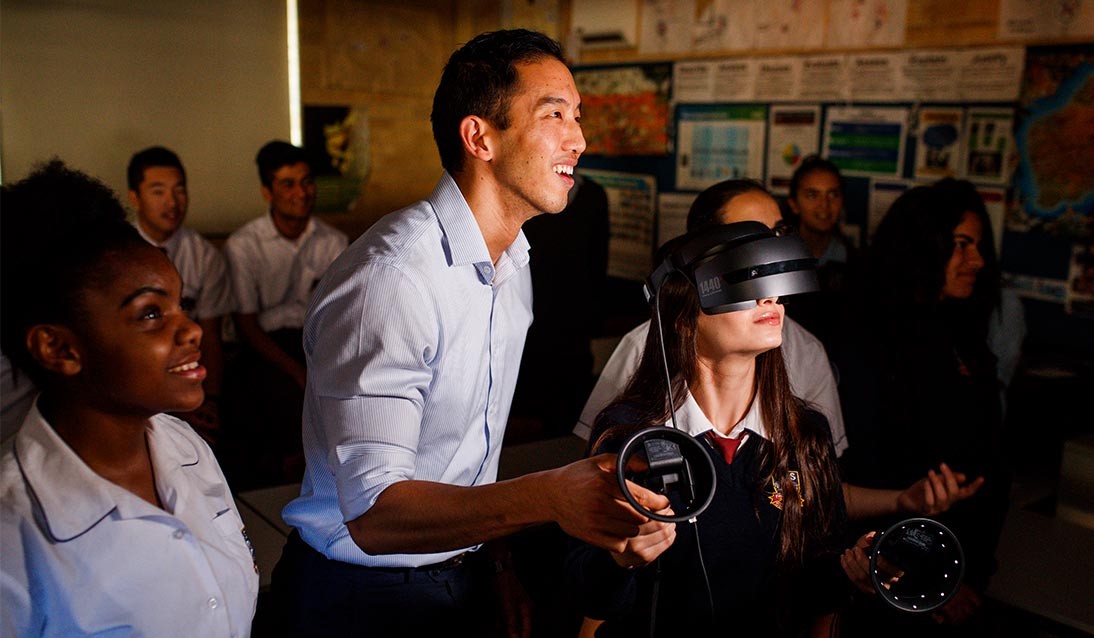 A teacher assists a student using a virtual reality headset and controllers.