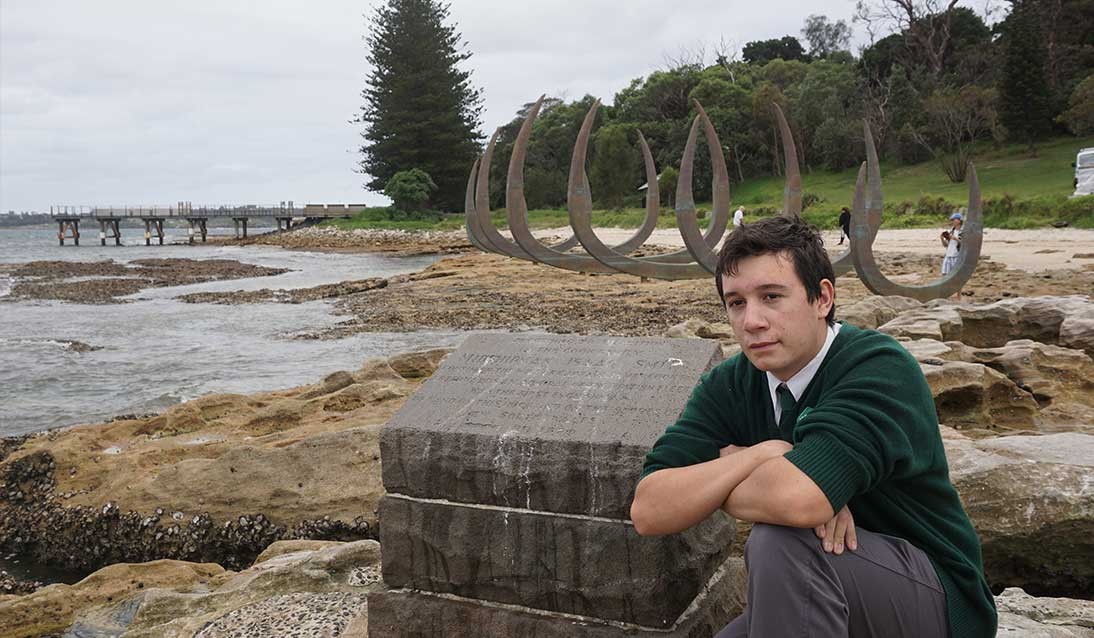 A boy sitting by a sculpture on the beach.