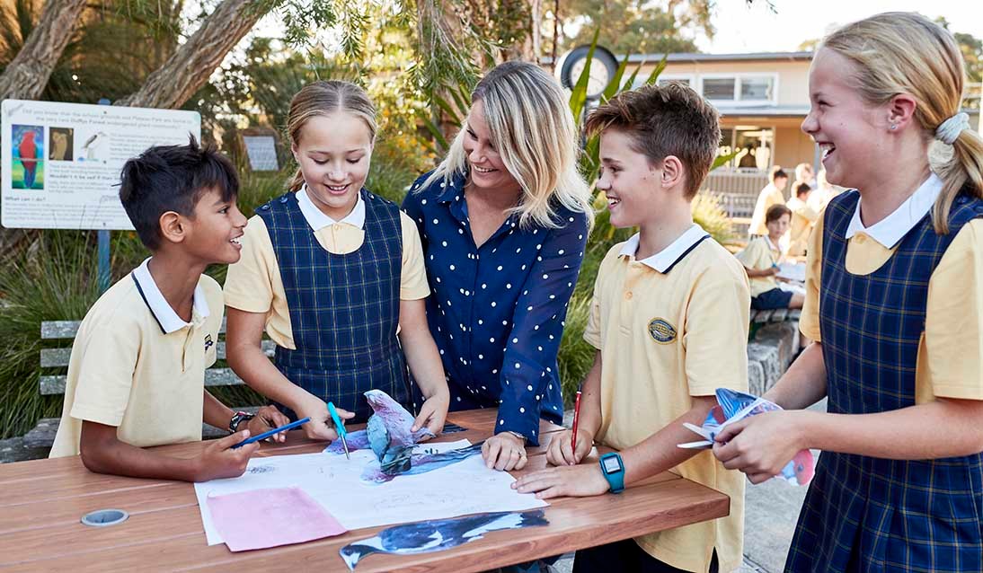 Female teacher with four primary students outside cutting out animal shapes from magazines.