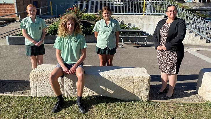 Three students, two standing and one sitting, with their principal.