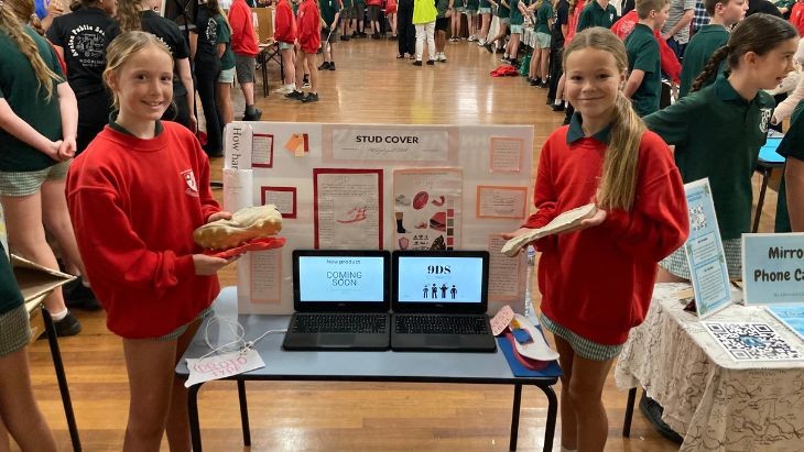 Two girls holding football boots in front of a display on a table.