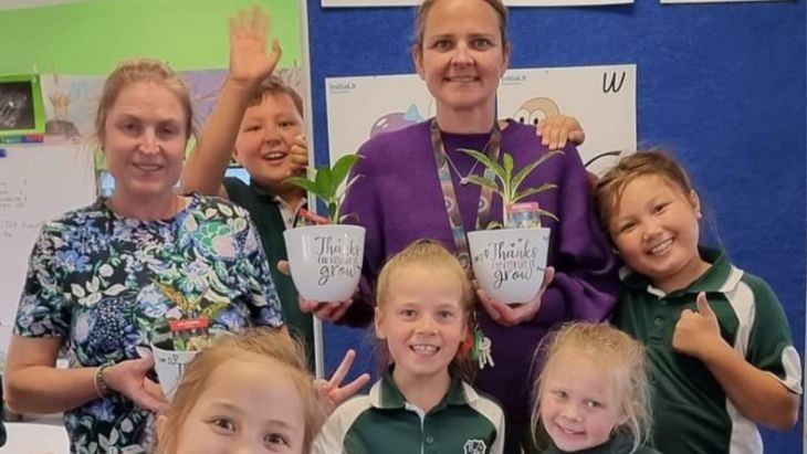 Students and teachers in a classroom holding pot plants.