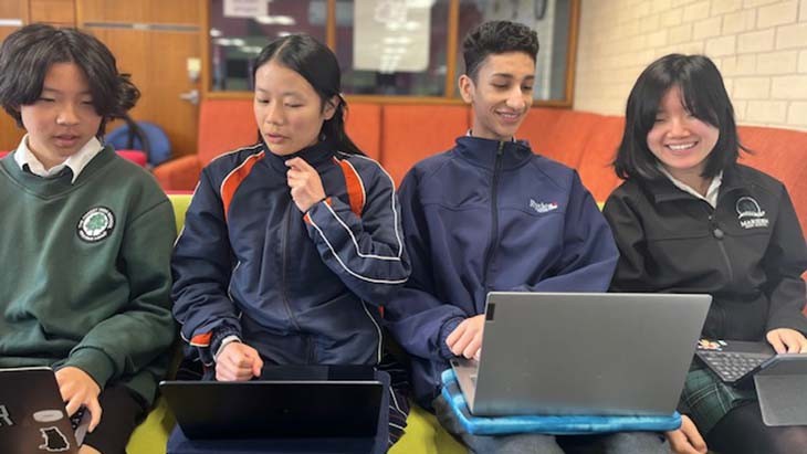 Four students sitting on a couch looking at laptops.