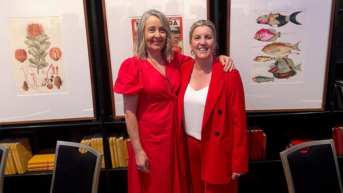 Two women in red clothing standing arm in arm