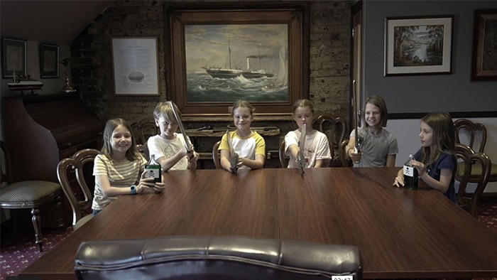 A group of six primary aged students sitting around a large table holding swords and poison.