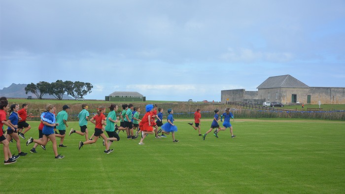 Students running in a field past a large stone historic building