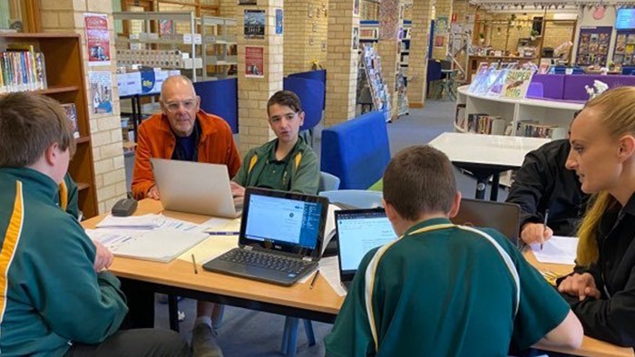A group of students and two teachers working together at a library table.